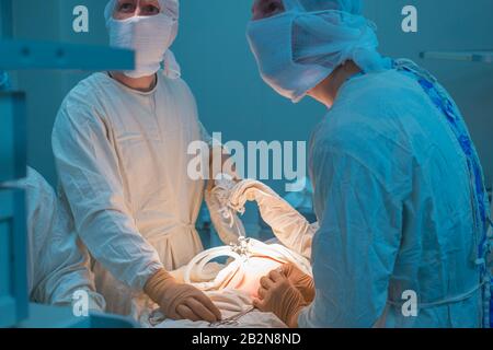 Nahaufnahmen von pädiatrischen Chirurgen, die eine Operation mit laparoskopischen Ports für die endoskopische Operation durchführen, mit Blick auf den Monitor. In sterilem Operatin Stockfoto
