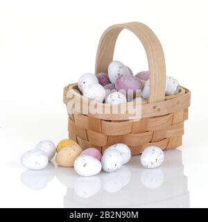 Ein Holzkorb mit kleiner easter Ei-Süßigkeit auf Weiß mit Spiegelung Stockfoto