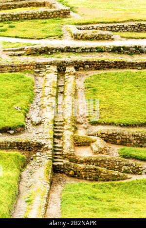Ein Blick aus der Vogelperspektive auf alte Steinruinen mit Terrassenstrukturen mit niedrigen Steinmauern und Wegen. Die Ruinen sind teilweise mit grünem Gras und Moos bewachsen, was das Alter und die Exposition gegenüber dem anzeigt Stockfoto