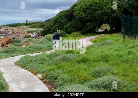 Frau, die auf dem Küstenweg bei der kleinen Siedlung in Onrus bei Hermanus, Provinz Westkap-Provinz, Südafrika, spazieren geht Stockfoto