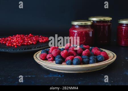 Hausgemachte Marmelade mit frischen Blaubeeren, Himbeeren und Rotkräuseln, dunkle Kulisse Stockfoto