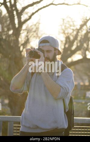 Europäischer Mann fotografiert/ Mann mit grauem Hut fotografiert/ Fotograf macht seine Arbeit/ Junger Mann mit Bart mit dslr-Kamera Stockfoto