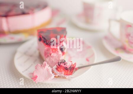 Untertasse mit Schwärzen-Käsekuchen und Löffel auf einem weißen Tisch Stockfoto