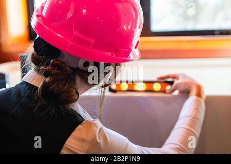 Kontrolle der Bauqualität: Nahaufnahme der Rückansicht einer Frau bei der Arbeit, sie verwendet eine Wasserwaage auf einer horizontalen Fläche im Innenbereich des Hauses. Stockfoto