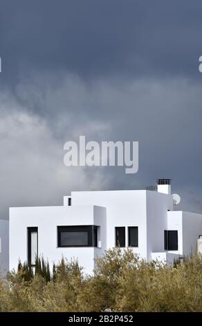 Blick auf ein weißes modernes Einfamilienhaus hinter Olivenbäumen Mit dunklen Wolken im Hintergrund in Andalusien Stockfoto
