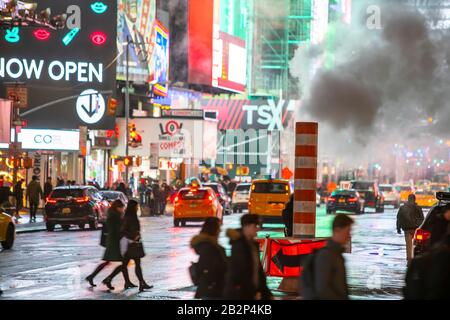 Der Verkehr geht durch und die Menschen überqueren die Avenue unter treibendem Dampf in der regnerischen Nacht am Times Square in Midtown New York City, New York, New York, USA, am 25. Februar 2020. Stockfoto