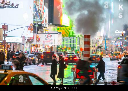 Der Verkehr geht durch und die Menschen überqueren die Avenue unter treibendem Dampf in der regnerischen Nacht am Times Square in Midtown New York City, New York, New York, USA, am 25. Februar 2020. Stockfoto