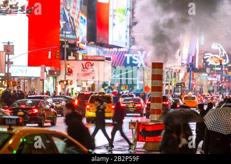 Der Verkehr geht durch und die Menschen überqueren die Avenue unter treibendem Dampf in der regnerischen Nacht am Times Square in Midtown New York City, New York, New York, USA, am 25. Februar 2020. Stockfoto