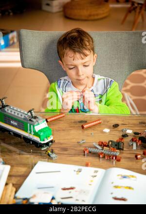 Junger Junge sitzt am Tisch, die Zusammenstellung Modell Zug aus Kunststoff-Bausteine. Stockfoto