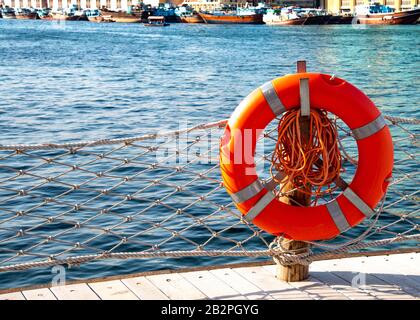 Orangefarbener Rettungsring am Wasserrand. Mit Kopierbereich. Stockfoto