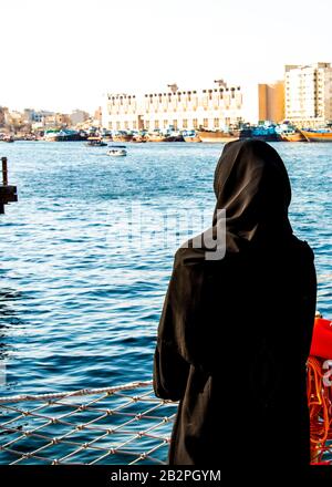 Rückansicht der Frau in schwarzem traditionellen Abaya mit Blick über den Dubai Creek VAE Stockfoto