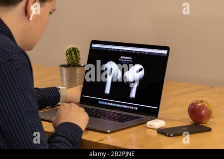 Mann, der sich den neuen Apple AirPods Pro auf der Apple-Website über ein Macbook Pro ansieht. Stockfoto