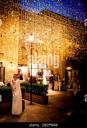 Farbbild eines Mannes, der in voller Länge steht, in traditioneller arabischer Kleidung gekleidet, mit Foto einer Lichtanzeige in der Nacht.Old Town, Dubai. Stockfoto