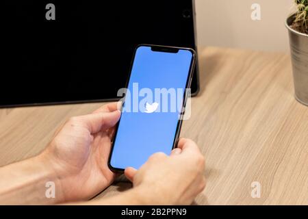 Mann sitzt an einem Tisch mit einem iPhone mit einem blau-weißen Twitter-Logo auf dem Bildschirm. Stockfoto