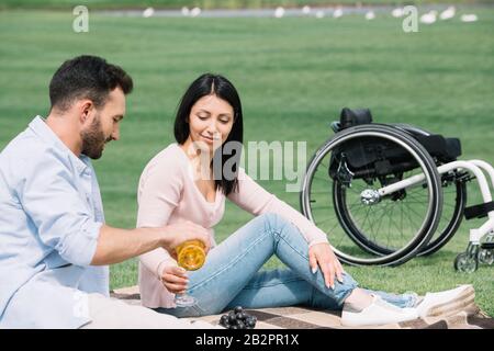 Gutaussehender Mann, der im Park mit behinderter Freundin Weißwein in Glas gießt Stockfoto