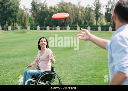 Junger Mann, der fliegende Scheibe zur behinderten Freundin im Park wirft Stockfoto