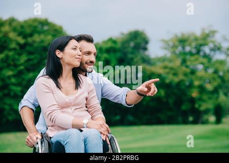 Fröhlicher Mann, der mit dem Finger zeigt, während er mit behinderter Freundin im Park spazieren ging Stockfoto