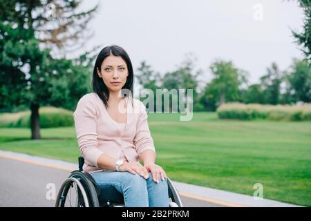 Pensive behinderte Frau, die im Rollstuhl im Park auf die Kamera blickt Stockfoto