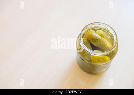 Eingepickte Gurken in offenem Glas in der Nähe des Tisches. Stockfoto