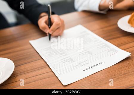 Selektiver Fokus des Mannes, der einen Vertrag über eine Autoversicherung im Autoshowroom unterzeichnet Stockfoto