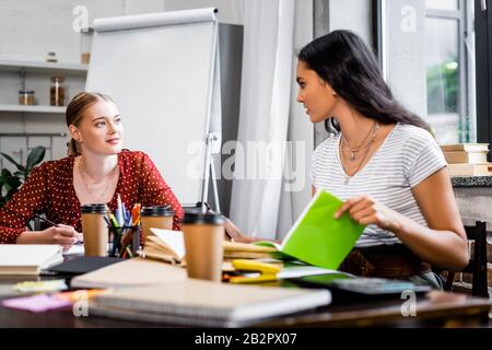 Attraktive multikulturelle Freunde, die am Tisch sitzen und in der Wohnung studieren Stockfoto