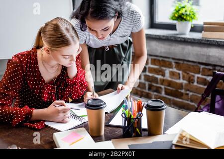 Attraktive multikulturelle Freunde, die am Tisch sitzen und in der Wohnung studieren Stockfoto