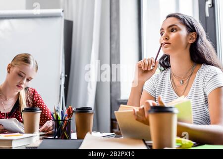 Attraktive multikulturelle Freunde, die am Tisch sitzen und in der Wohnung studieren Stockfoto