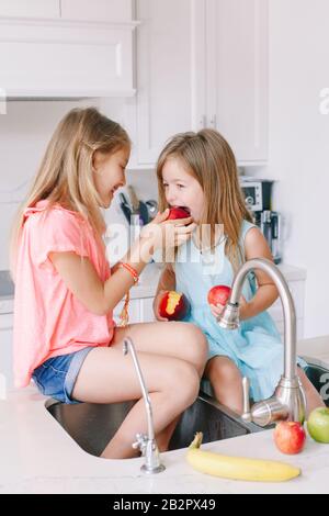 Kaukasische Kinder Mädchen, die frische Früchte essen, die in der Küchenspüle sitzen. Glückliche Geschwister der Familie, die einen Imbiss haben. Organische Lebensmittel gesund delicio Stockfoto