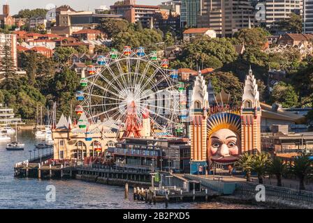 Sydney, Australien - 11. Dezember 2009: Nahaufnahme der farbenfrohen Attraktionen der Luna Park Messe mit Kirribilli Baudngs im Rücken. Etwas grünes Laub. Stockfoto