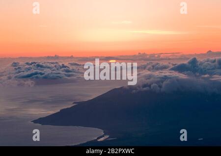 Oben auf Haleakala, beobachten Sie, wie sich die Sonne von über den Wolken und über der Maui-Küste verlangsamt. Stockfoto