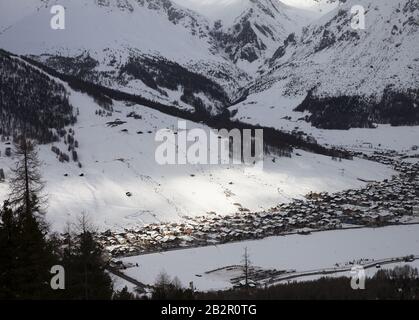 Verschneite Skipiste mit Seilbahnen und Stadt im Bergtal am Winterabend. Italienische Alpen. Livigno, Region Lombardei, Italien, Europa. Draufsicht von Stockfoto