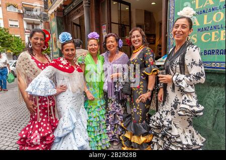 Eine Gruppe von Frauen, die während der Aprilmesse in Sevilla, Spanien, bunte Flamenco-Kleider vor einer Bar tragen Stockfoto