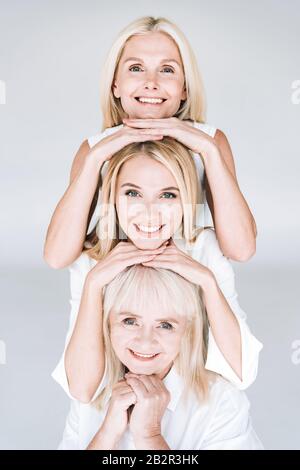 Schön lächelnde, dreigenerationenblonde Frauen isoliert auf Grau Stockfoto