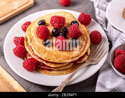 Süße hausgemachte Pfannkuchen mit Himbeeren und Blaubeeren auf weiße Platte. Stockfoto