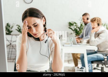 Attraktiver Makler mit Kopfschmerzen in der Nähe von Mitarbeitern im Büro Stockfoto