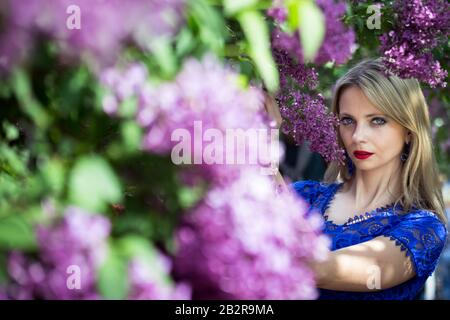 Blondes Mädchen im aufblühenden Flieder, horizontale Ausrichtung, Blick auf die Kamera. Stockfoto