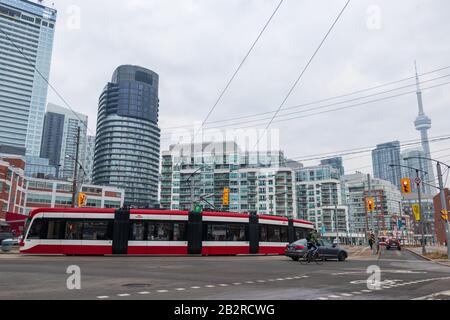 Eine Bombardier TTC Straßenbahn ist auf einer belebten Straße mit der Skyline der Stadt, CN Tower im Hintergrund zu sehen. Stockfoto