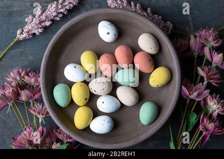 Ostereier in Pastellfarben auf einer alten Holzhintergrundstruktur gemalt, Betonplatte umgeben mit verschiedenen Frühlingsblumen in moderner Stockfoto