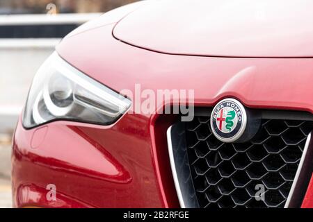 Alfa Romeo Emblem auf der Vorderseite eines roten Stelvio SUV an hellen Tag. Stockfoto