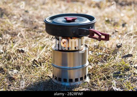 Camping Kochen im Freien auf Massivholzbrenner mit Feuer. Bratpfanne mit Blei darauf. Stockfoto