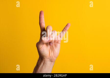 Rock it. Man Hand zeigt eine Geste mit Felszeichen über einem gelben Hintergrund mit dramatischem Schatten Stockfoto