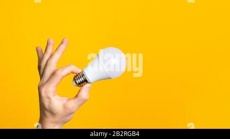 Close-Up man Hand hält weiße LED-Glühbirne vor gelbem Hintergrund. Konzept von ideal, Umweltökologie und Energieeffizienz Stockfoto