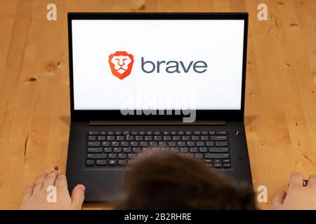 Ansicht von oben auf einen Mann, der an einem Schreibtisch sitzt und einen Laptop mit dem Brave Browser-Logo auf dem Bildschirm verwendet. Stockfoto