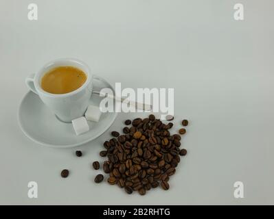 Eine Kaffeetasse mit Untertasse und Löffel neben ganzen Kaffeebohnen Stockfoto