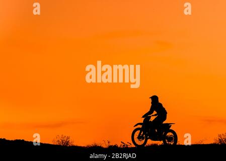 Schwarze Silhouetten Motocross-Fahrer auf einem Motorrad vor farbenfrohem Sonnenuntergang Stockfoto