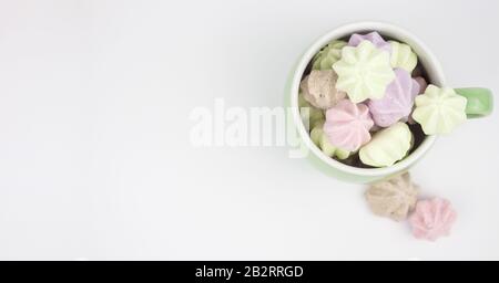 Marshmallow mehrfarbig. Meringue Marshmallows in einem grünen Becher auf hellem Hintergrund. Bunte Farbtöne auf weißem Hintergrund. Viele süße Marshmal Stockfoto