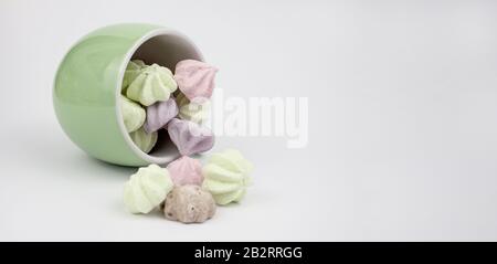 Marshmallow mehrfarbig. Meringue Marshmallows in einem grünen Becher auf hellem Hintergrund. Bunte Farbtöne auf weißem Hintergrund. Viele süße Marshmal Stockfoto