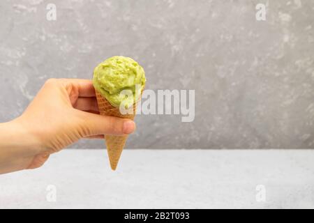 Frau hält einen Waffelkegel mit gesundem hausgemachtem Avocado-Eis auf neutralem Hintergrund mit Kopierraum Stockfoto