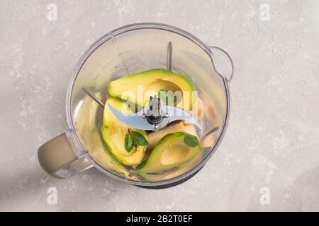 Mixer mit Avocado, gefrorenen Bananen- und Minzenblättern für Avocado-Eis auf neutralem grauem Hintergrund, Draufsicht Stockfoto