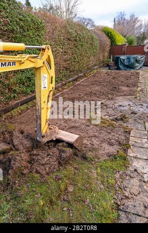 Cardiff, WALES - JANUAR 2020: Eimer und Arm eines Minibaggers, der den Rasen im Hintergarten eines Wohneigentums aufgräbt Stockfoto